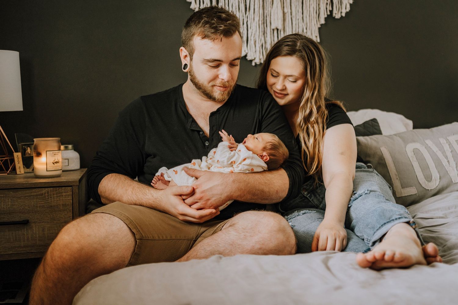 Parents share a quiet moment with their newborn on a cozy bed.