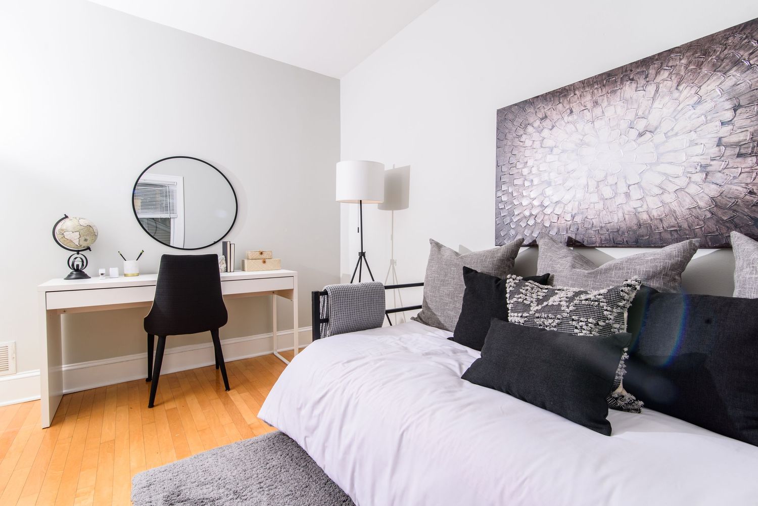 Modern bedroom with desk area, round mirror, and black and white wall art.