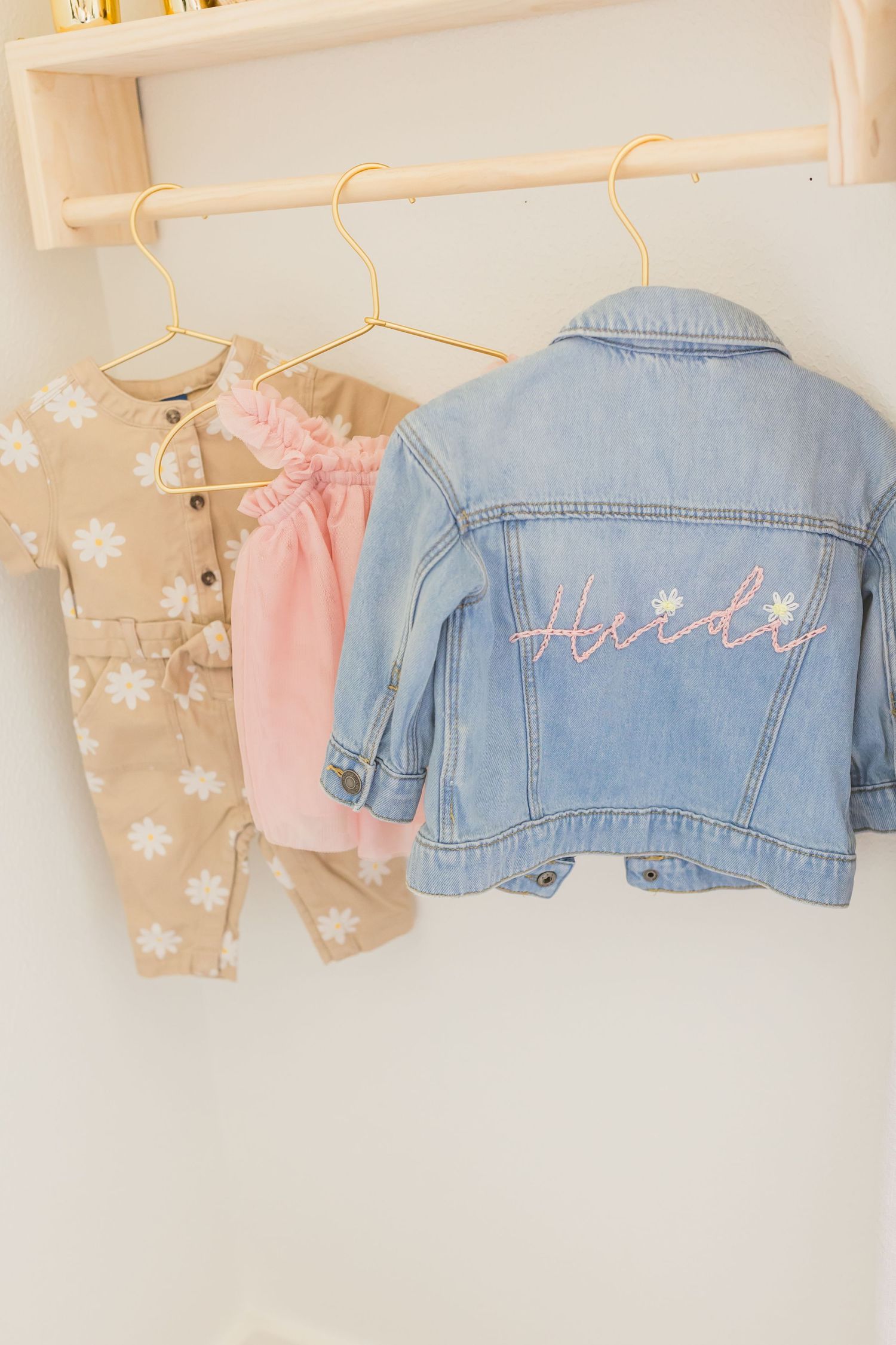 Baby clothes hanging on wooden rack including denim jacket and floral prints.