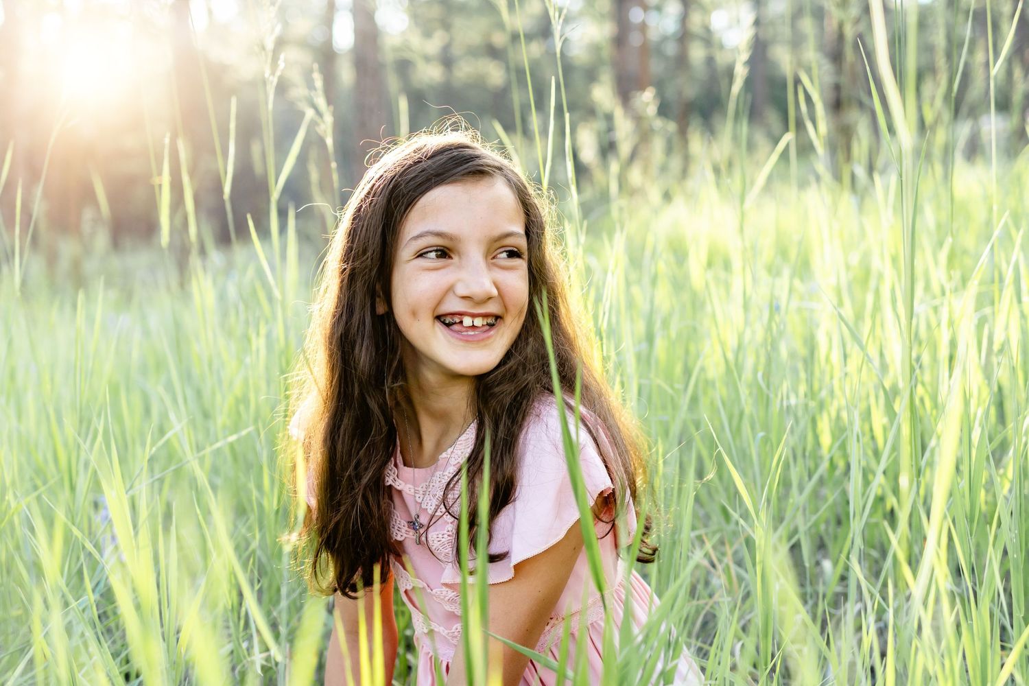 Young girl smiles at sunset sitting in the long grass during their family session in Colorado Springs.