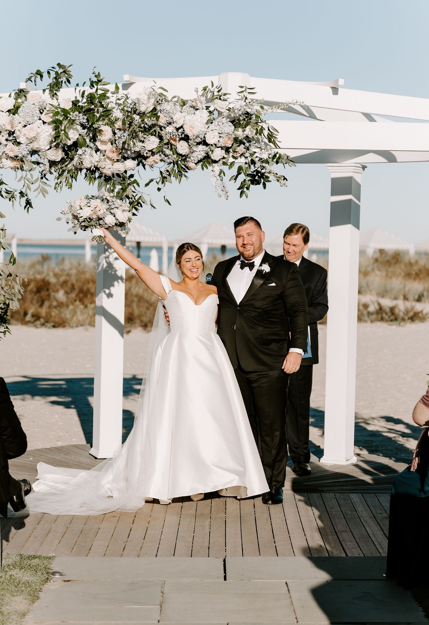 Couple celebrates their wedding day with joyful poses under an elegant white pergola.