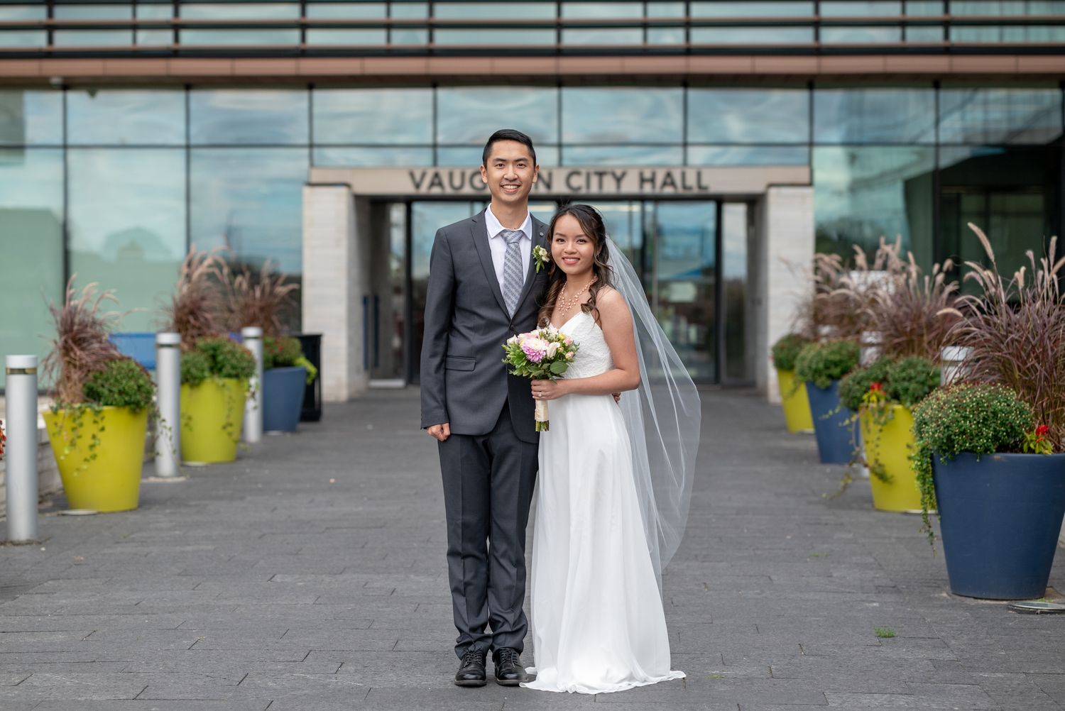 Newlyweds stand together in front of Vancouver City Hall entrance.
