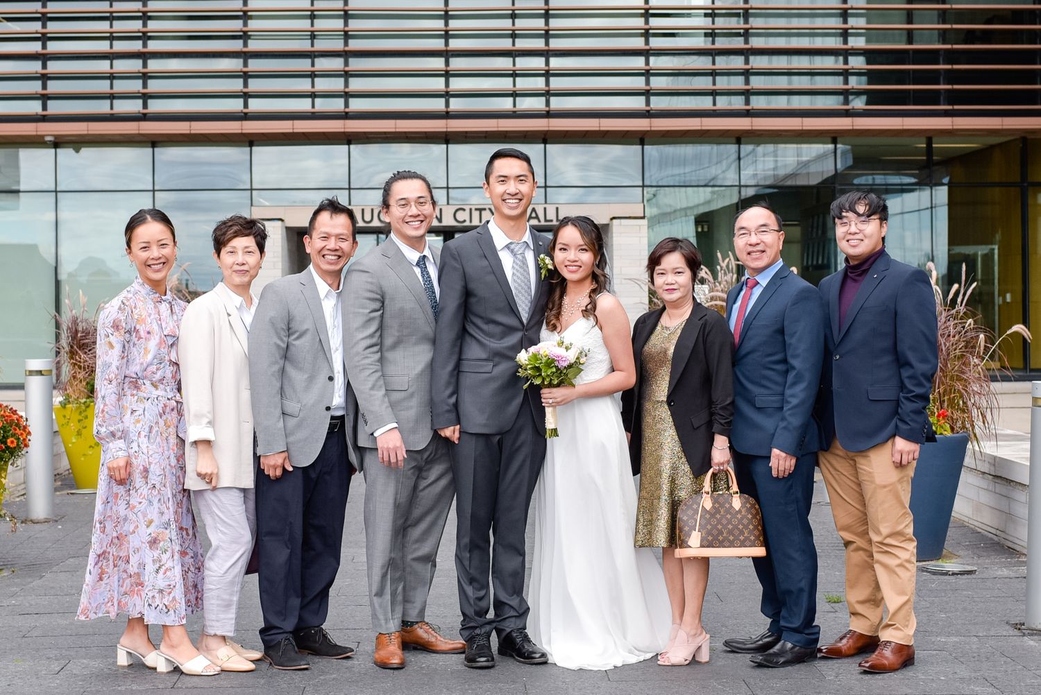 Wedding party poses together outside modern building entrance.
