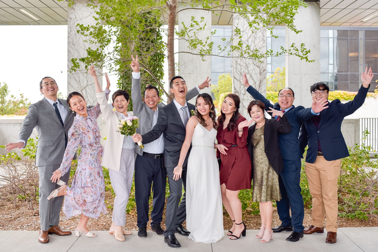 Wedding party group photo with friends celebrating joyfully outdoors with raised arms.