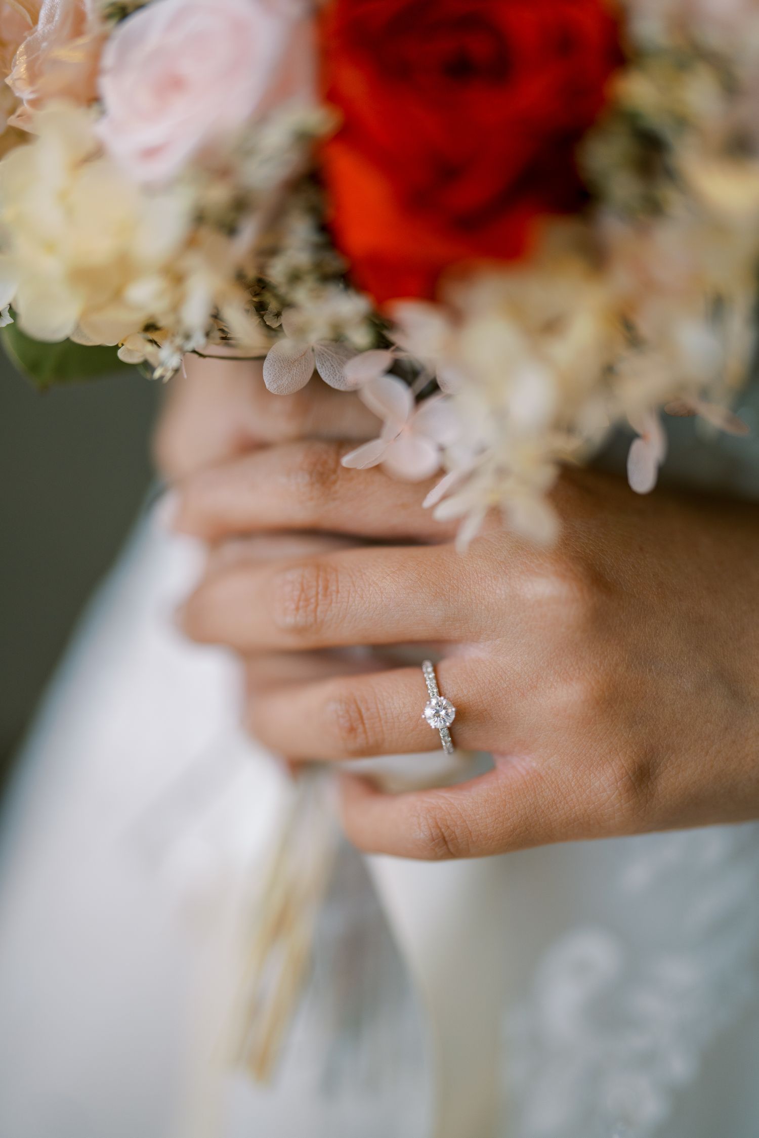Close-up shot of an elegant diamond engagement ring with floral bouquet in soft focus.
