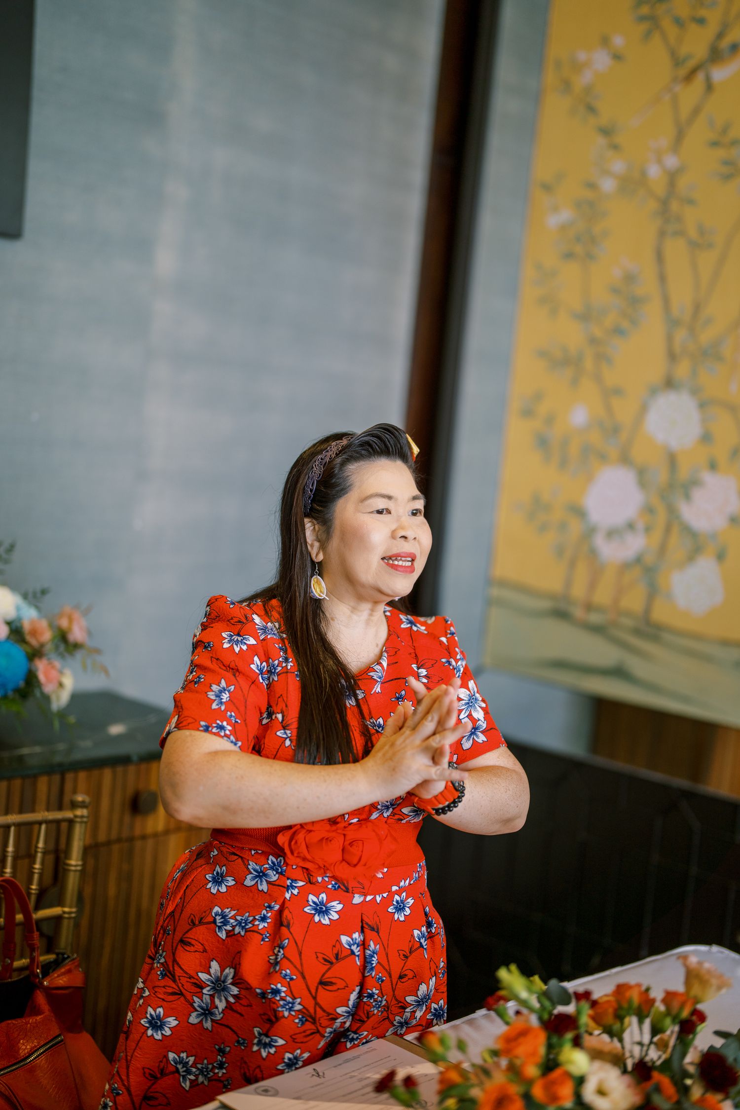 A woman in a vibrant red floral dress smiles during a wedding celebration.