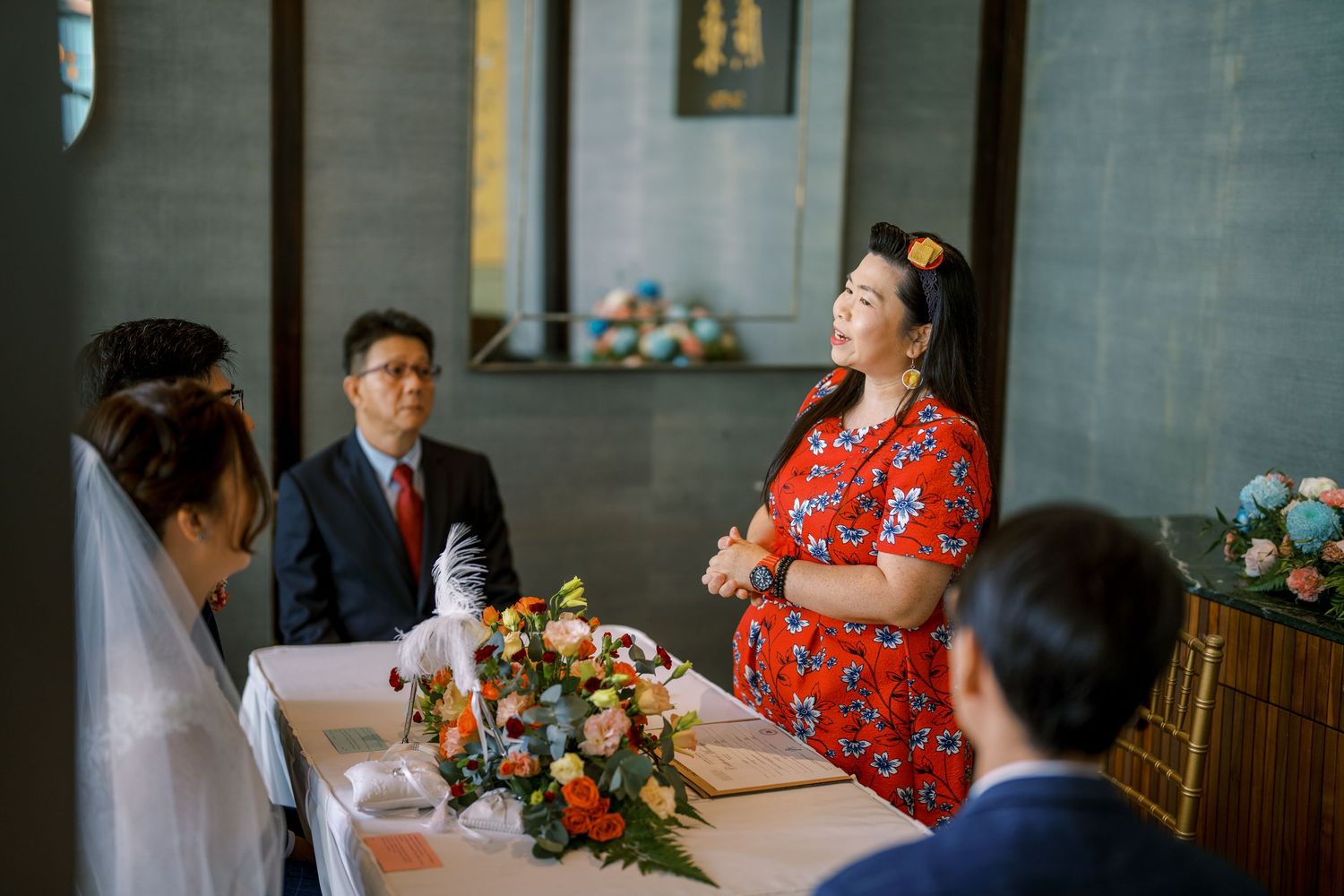 A wedding ceremony with someone in red delivering a speech at an elegant indoor venue.