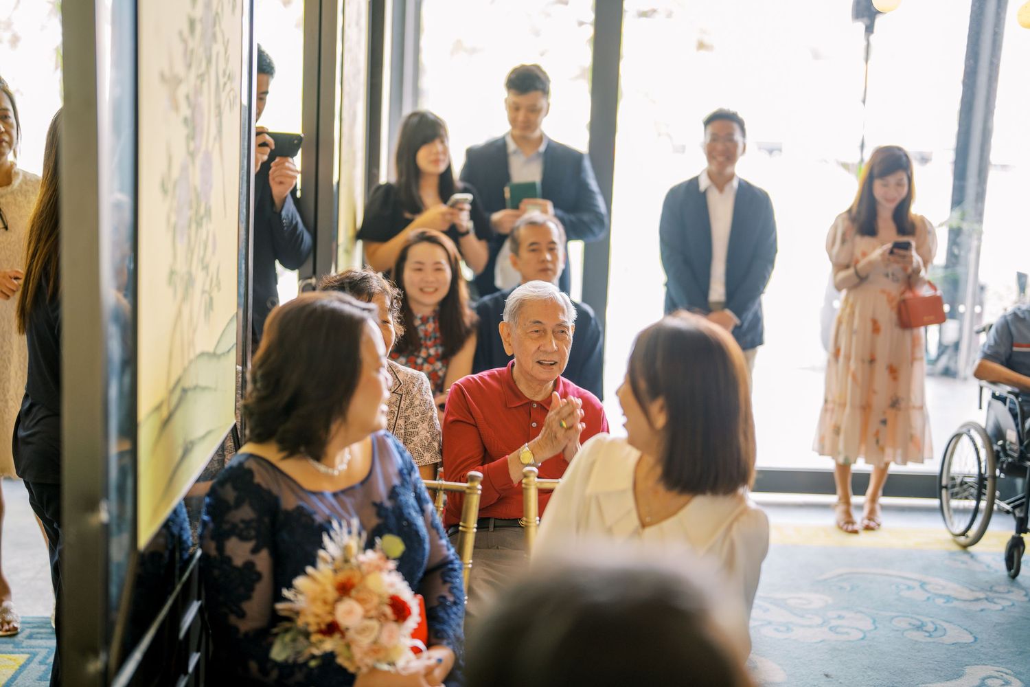 Wedding guests gather in a bright venue entrance with natural lighting and floral decorations.