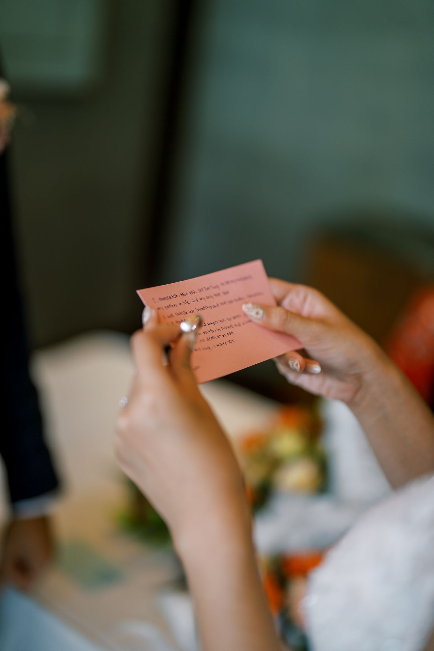 Close-up of hands holding a pink note card during a wedding ceremony.