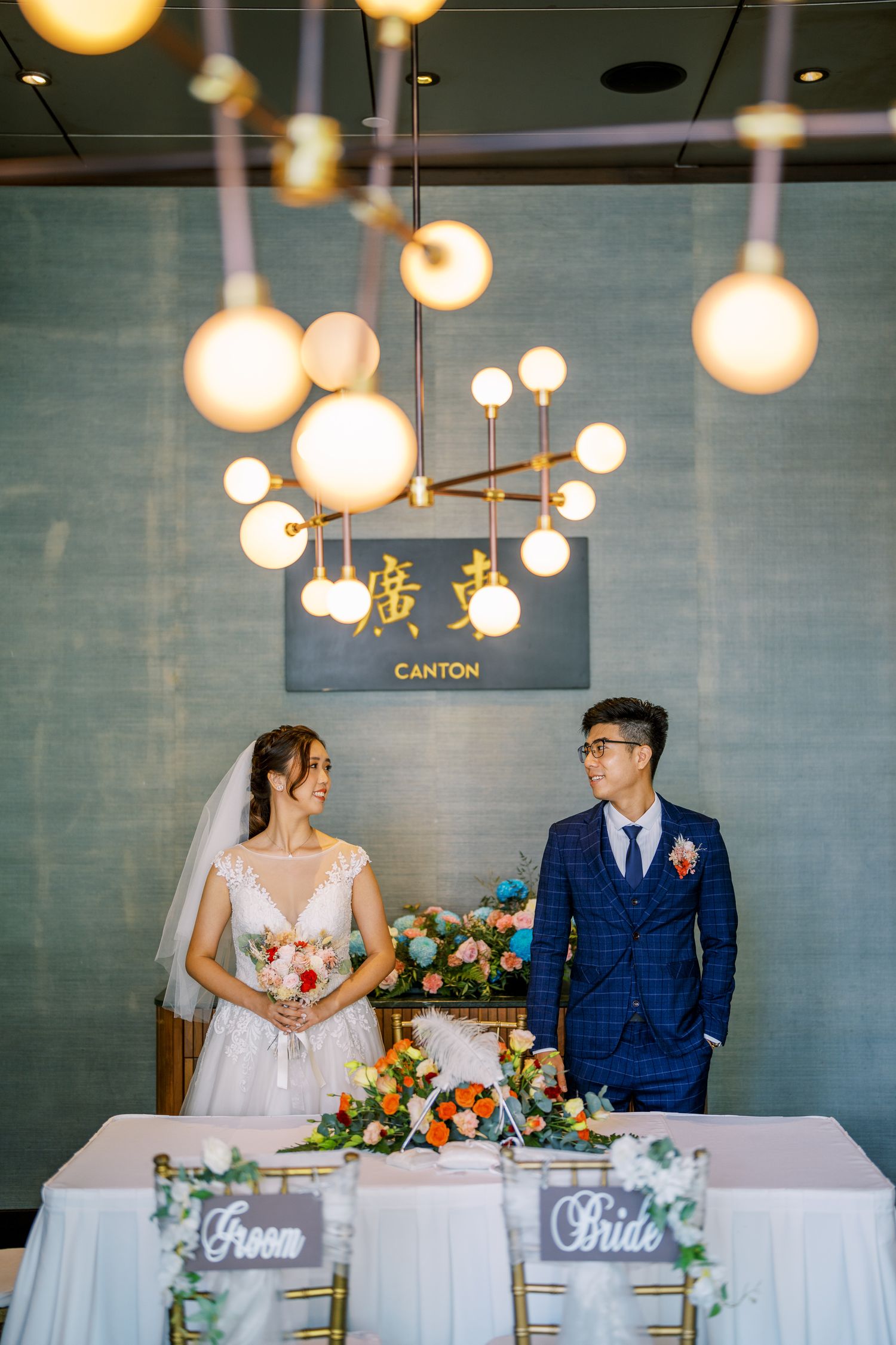 Wedding reception setup with elegant lighting and floral centerpieces on white-clothed tables.