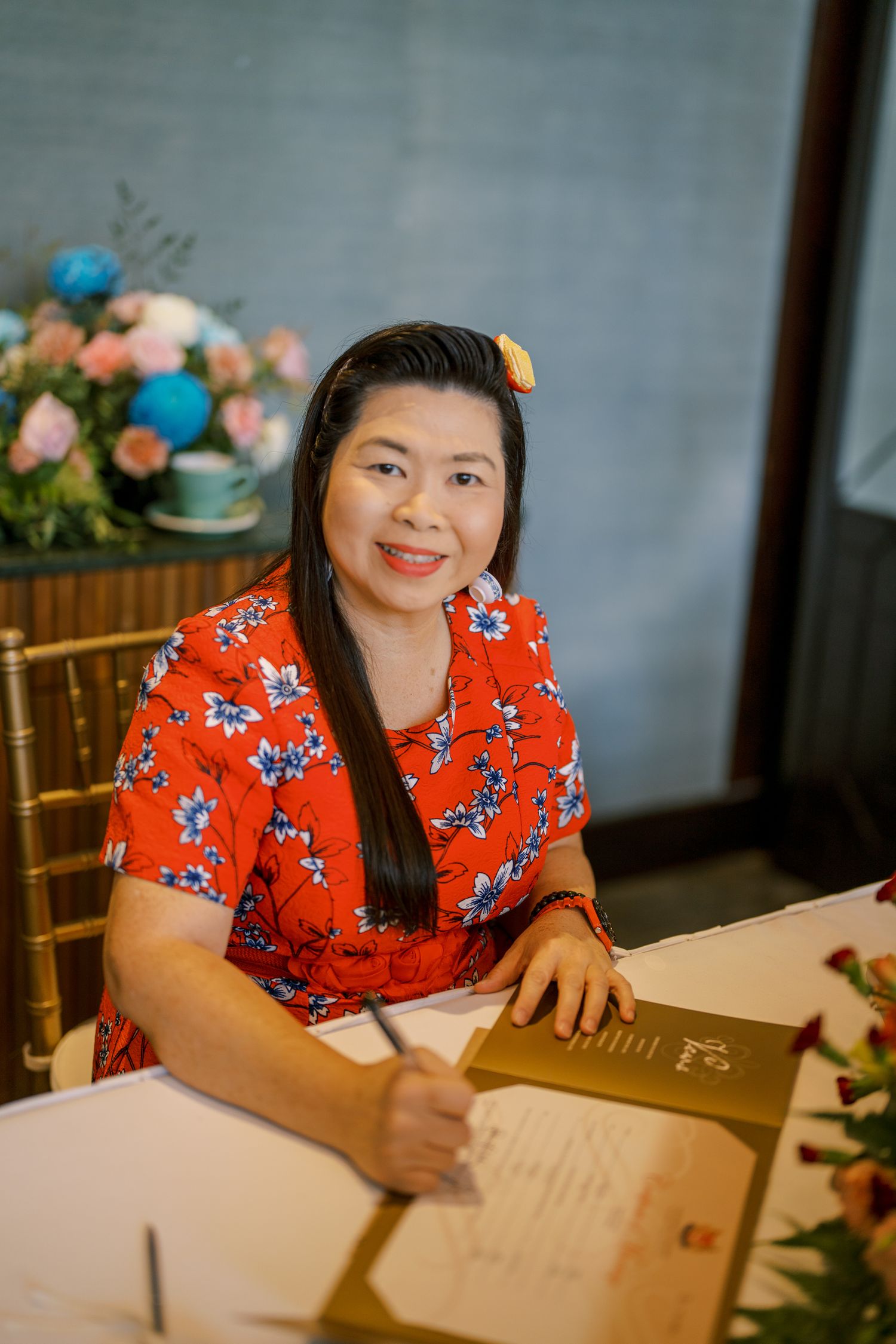 Guest in red floral dress signing a document at wedding reception.
