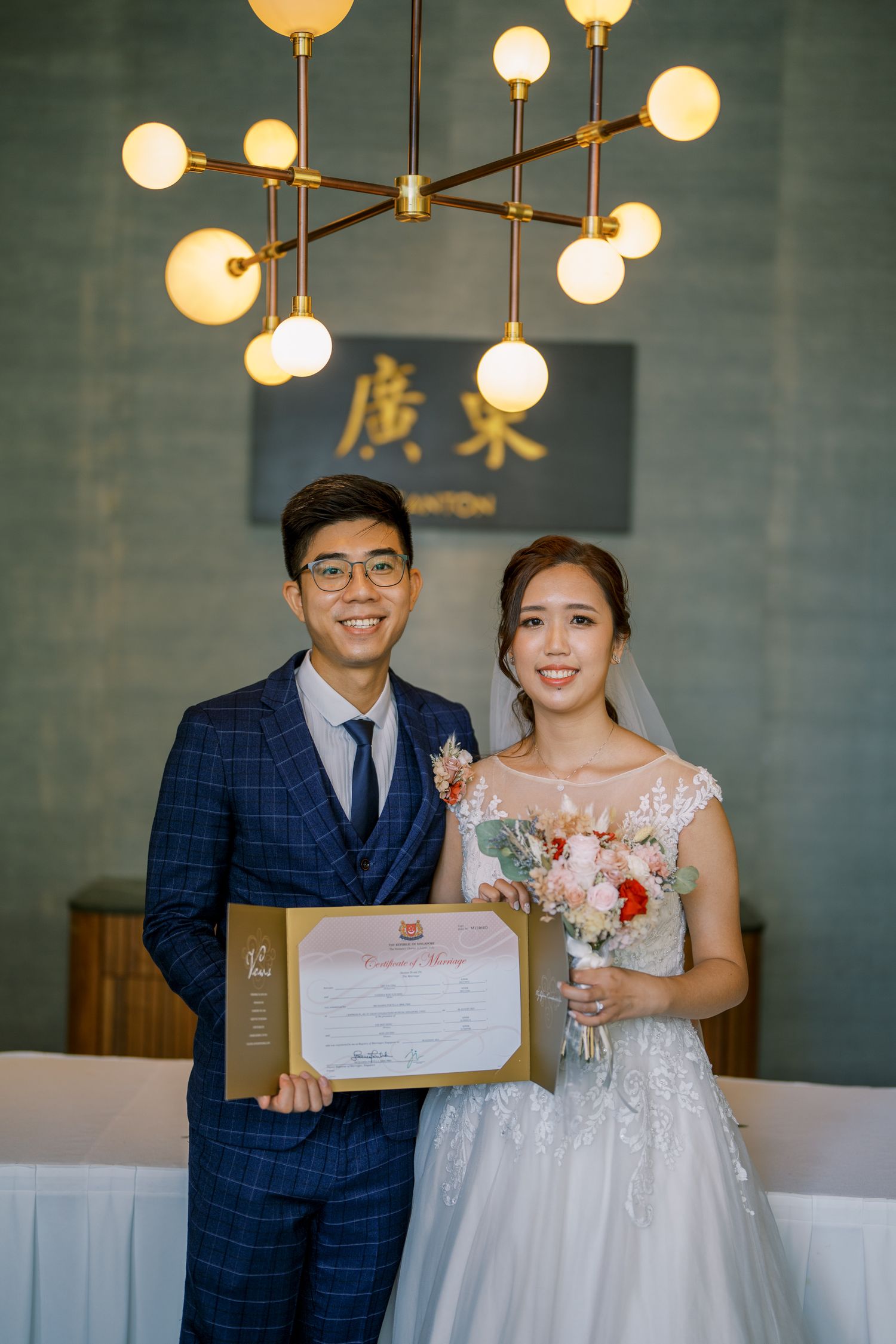 Newlyweds holding their marriage certificate under modern pendant lighting.