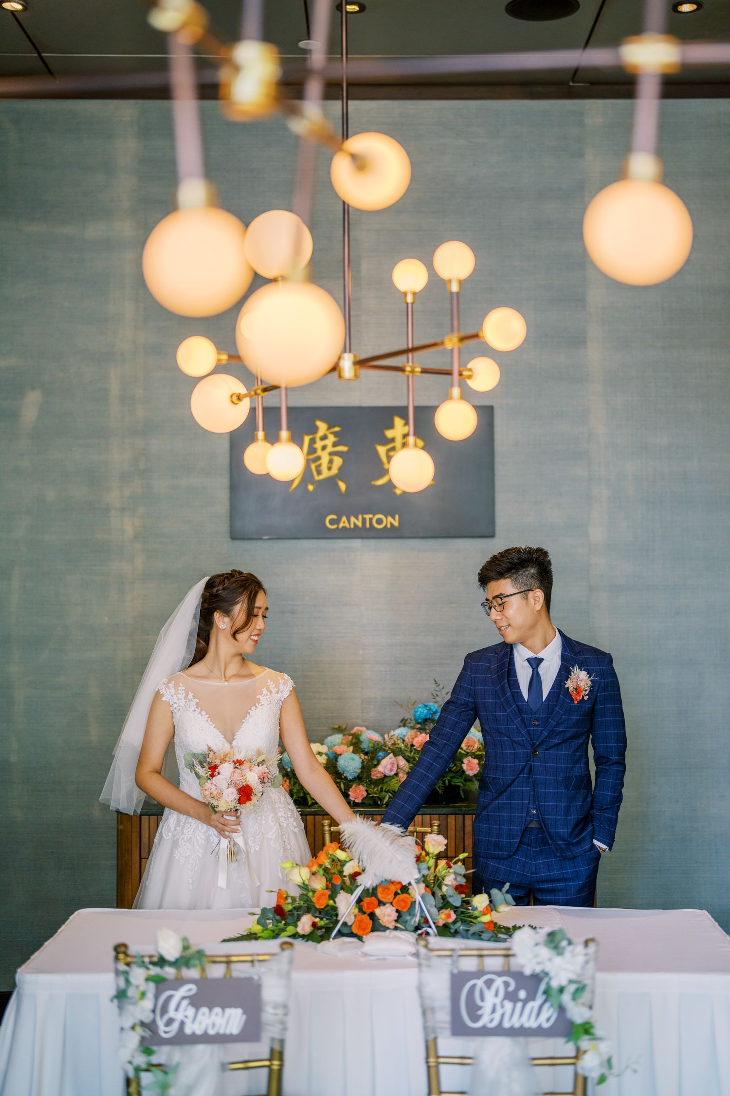 Newlyweds at their reception table with hanging globe lights and modern decor.