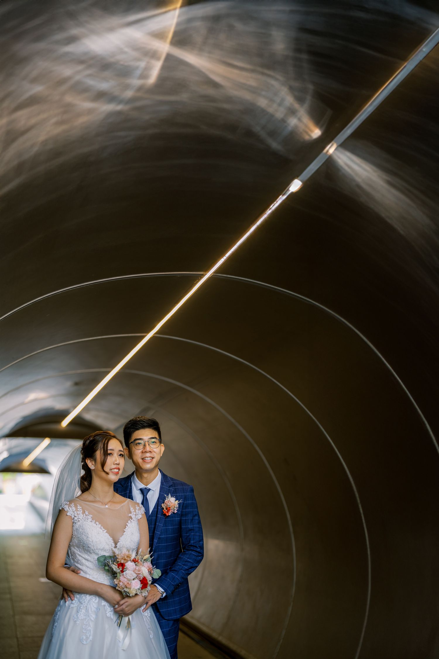 Creative wedding photo taken inside a curved tunnel with dramatic lighting effects.