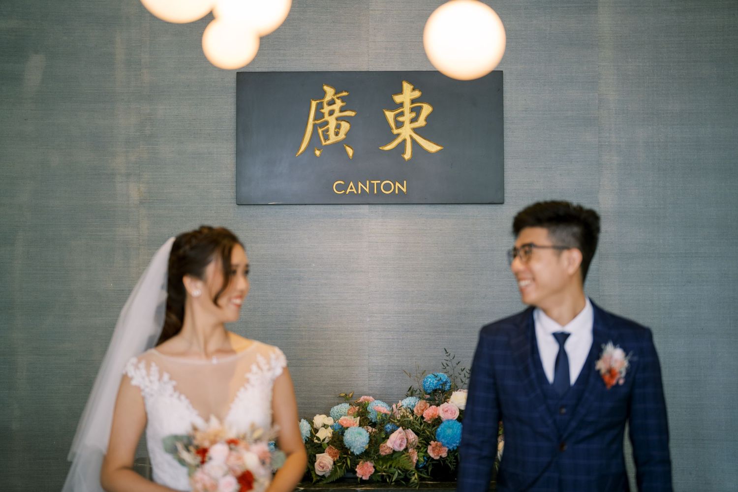 A wedding couple poses in front of an elegant Chinese restaurant sign with glowing lights.