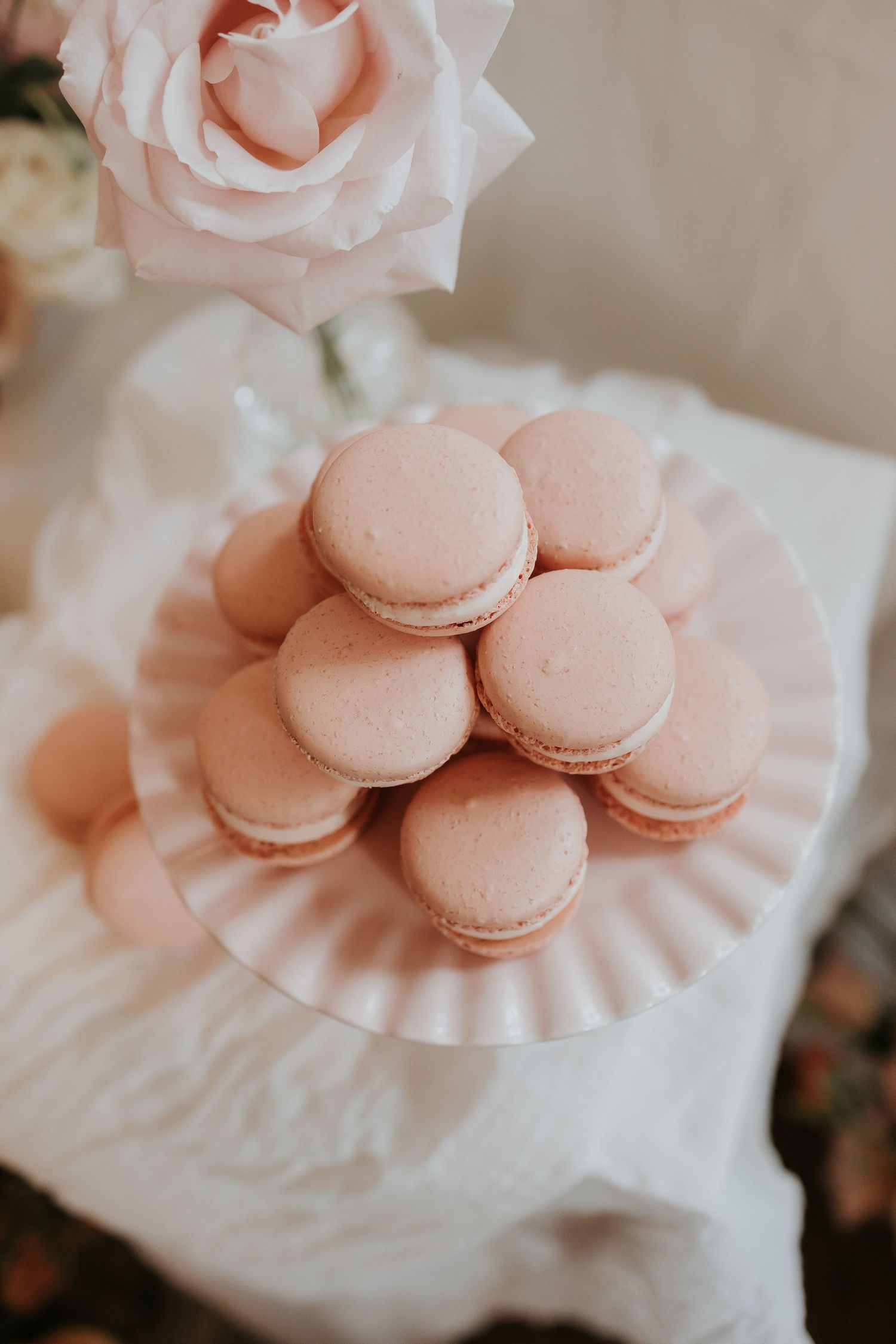 Pink macarons stacked on white plate with soft rose decoration.