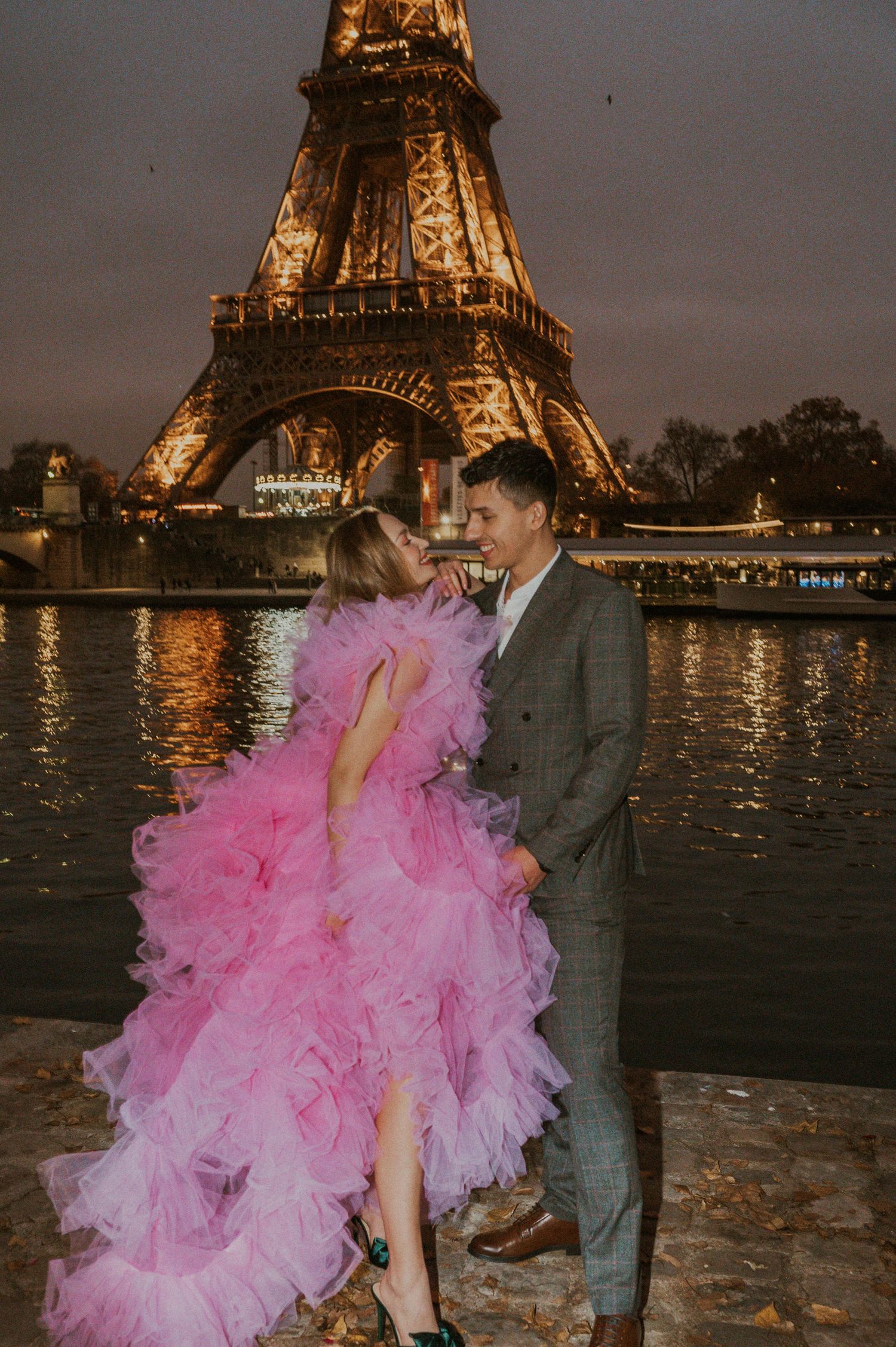 Couple sharing a romantic moment by the illuminated Eiffel Tower with one wearing a pink tulle dress.