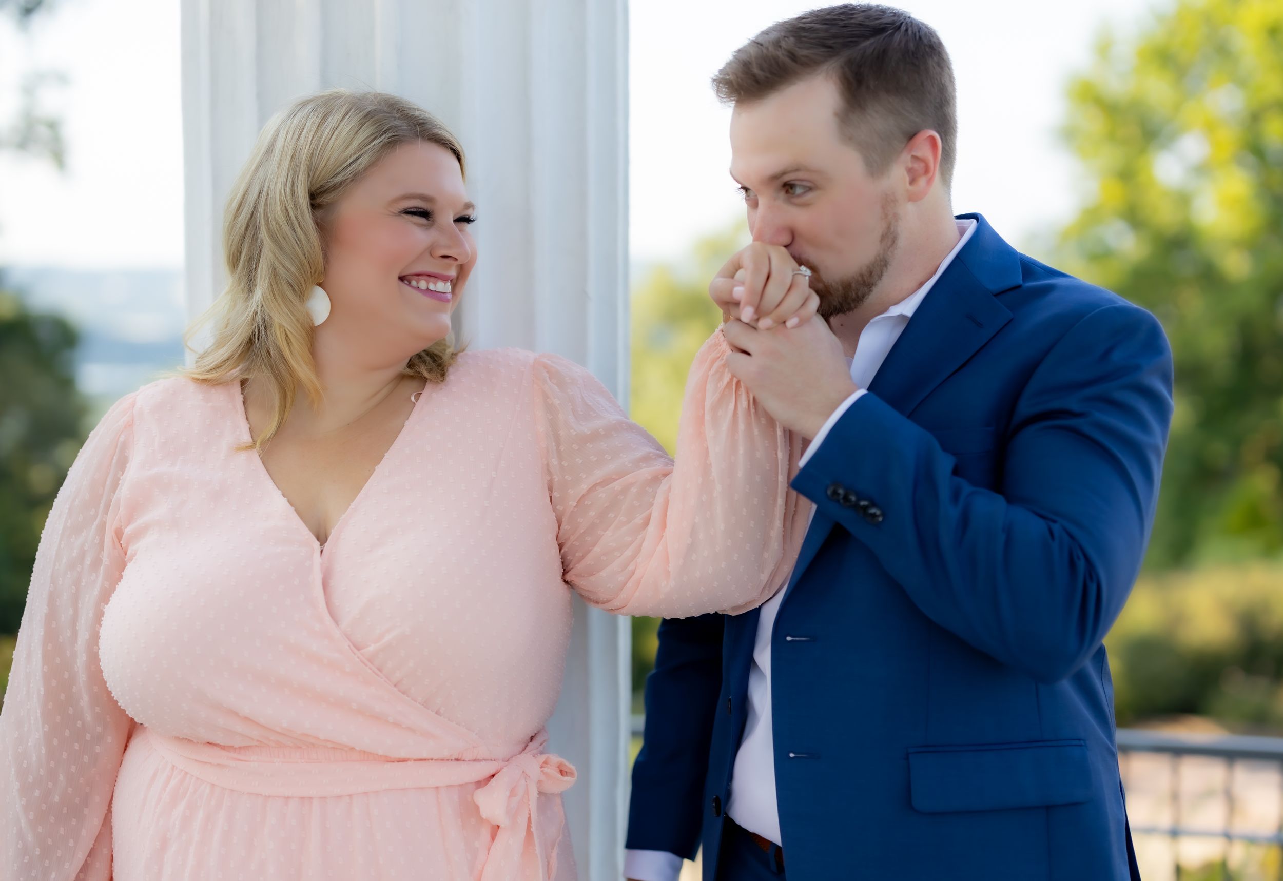 Couple shares tender moment outdoors near white columns.