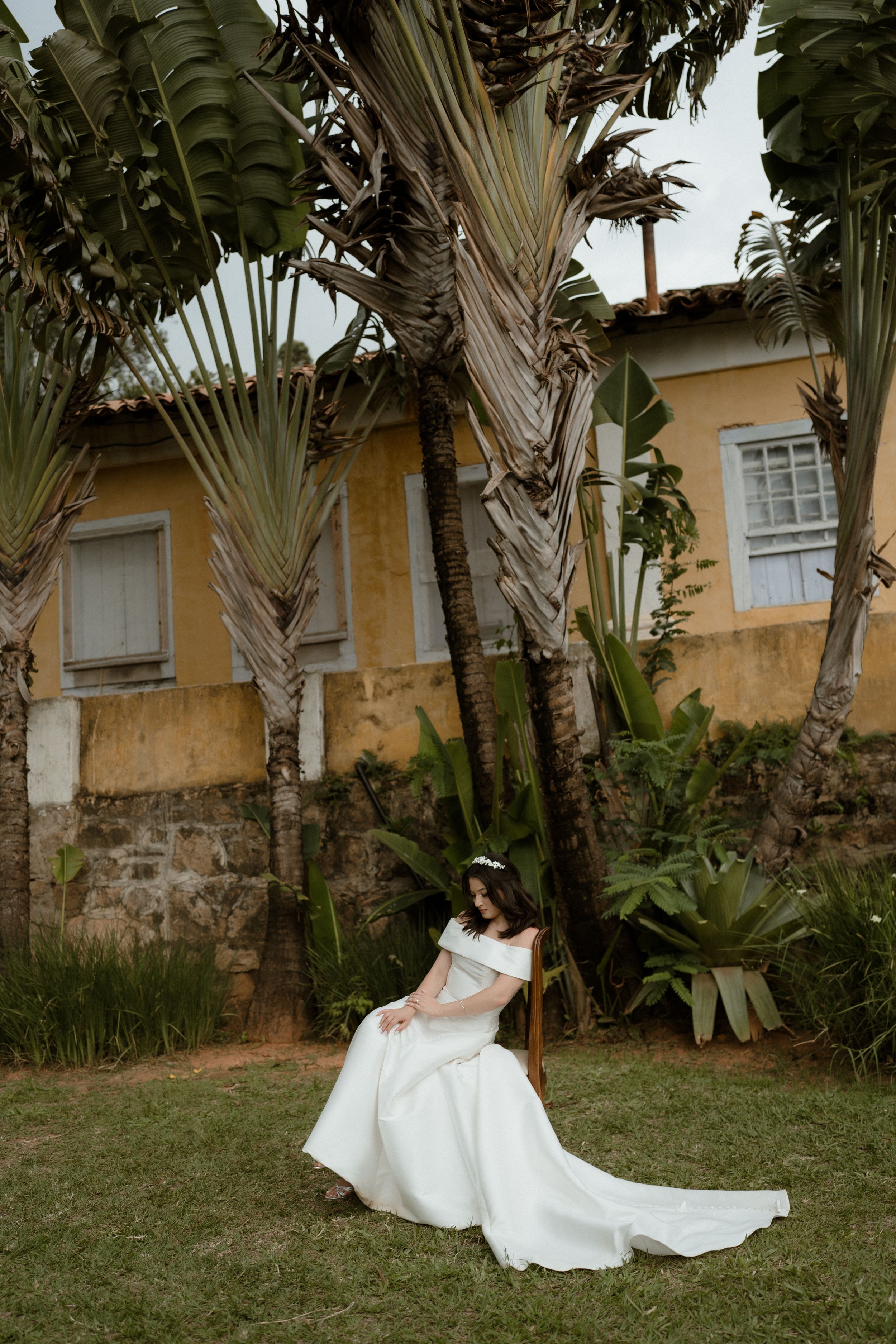 White wedding dress flows gracefully against tropical palm trees and yellow building backdrop.