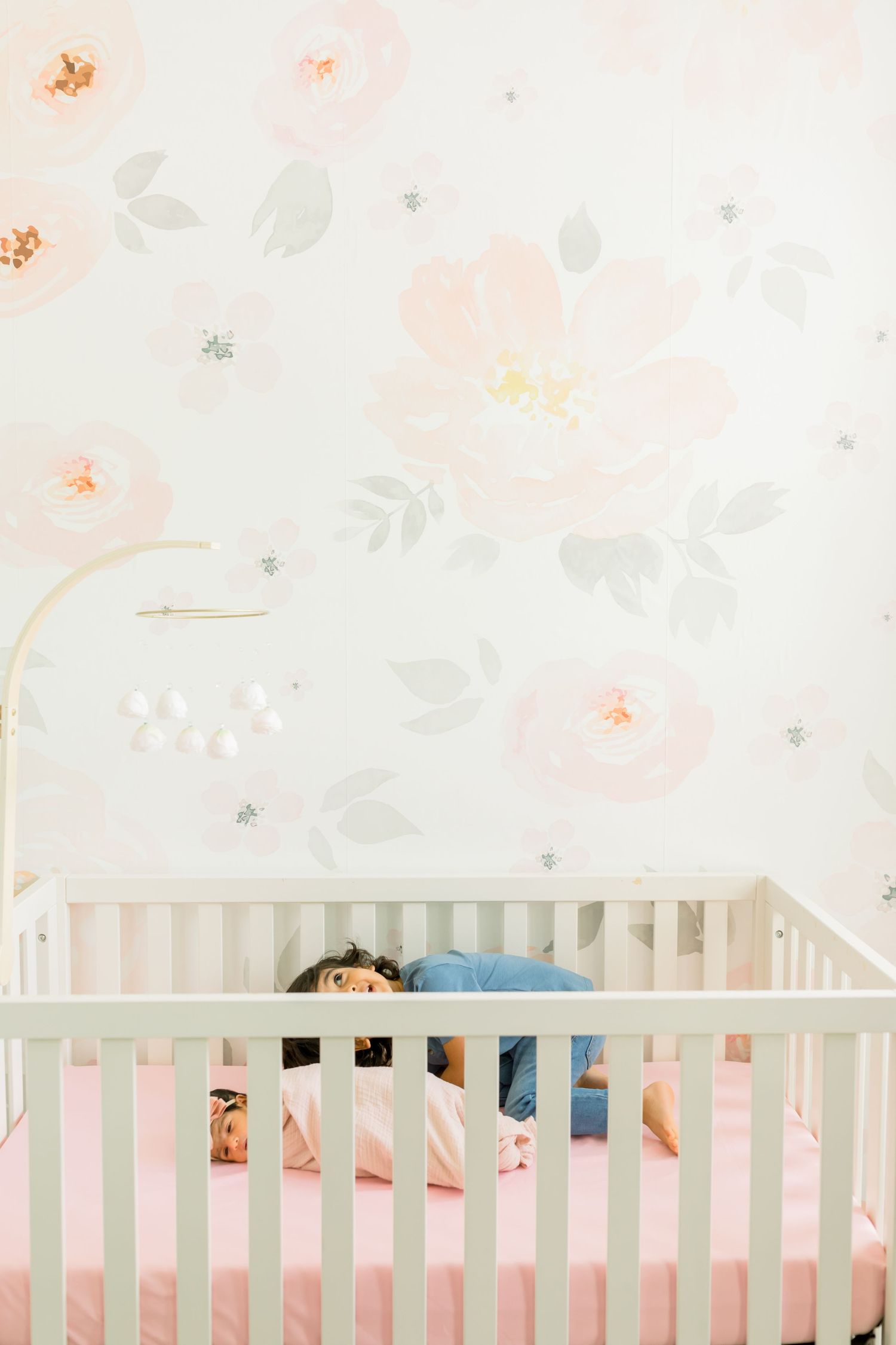 Top view of white crib with child peeking over the railing in floral-themed nursery.
