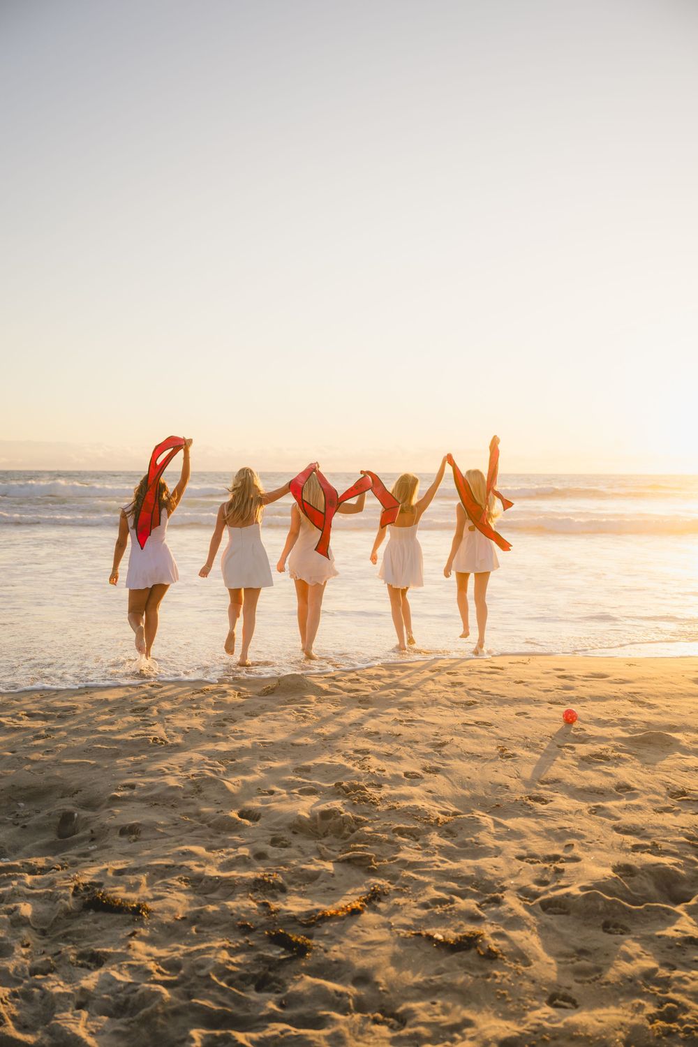 Group of SDSU graduates holding their stoles as they walk towards the ocean at Mission Beach to pose for grad photos.