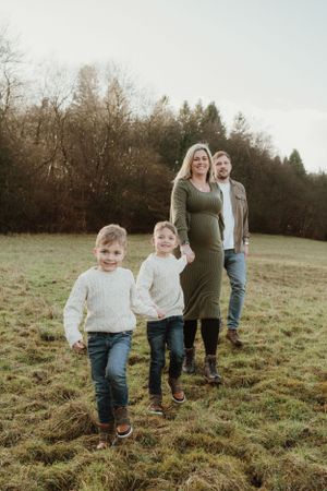 A family walks together across a grassy hillside during golden hour.