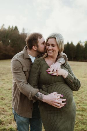 A couple shares an intimate embrace in a green sweater on a grassy field.