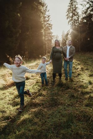 Family plays on a sunlit hillside among evergreen trees during golden hour.