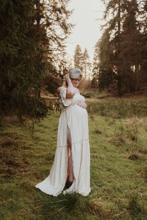 Two people in flowing white dresses embrace in a sunlit forest clearing.