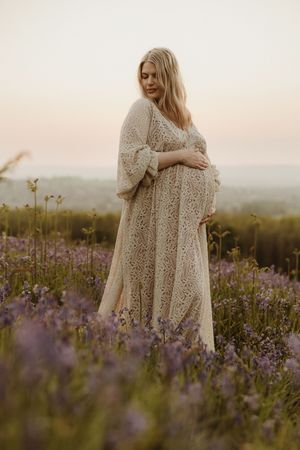 Woman in lace dress poses gracefully among purple wildflowers at sunset.