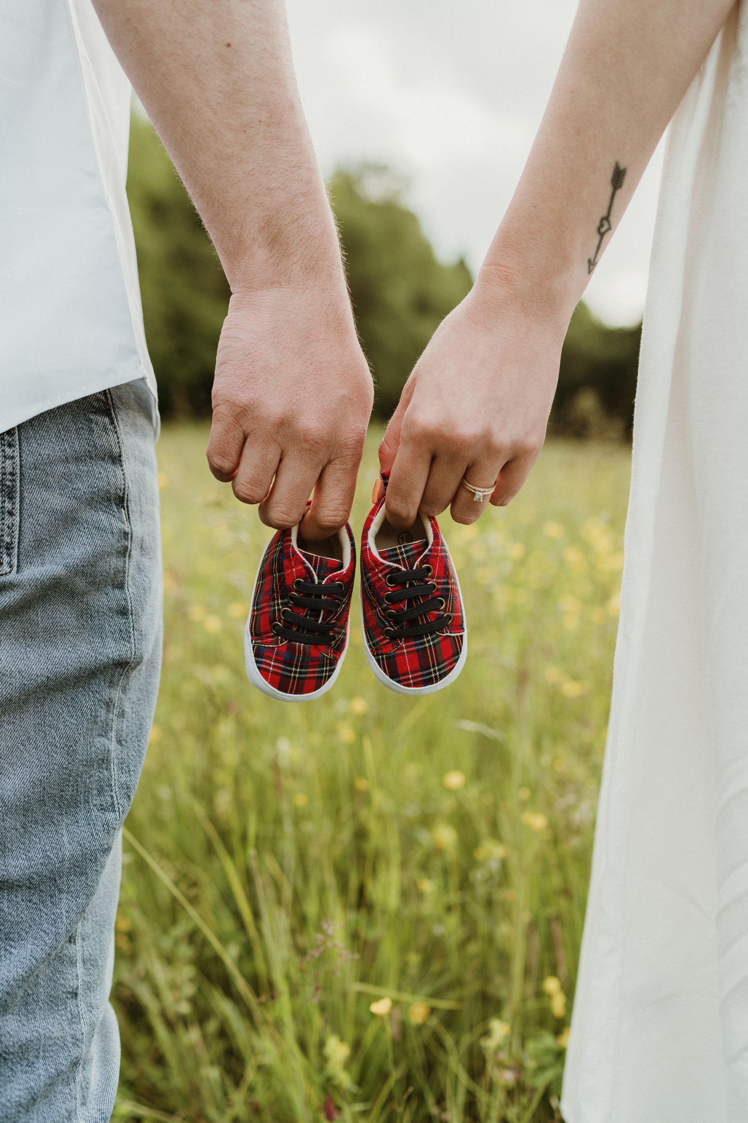 Hands holding small plaid baby shoes in flowering meadow.