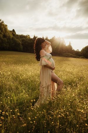 A maternity portrait in a golden field at sunset with wildflowers and dramatic lighting.