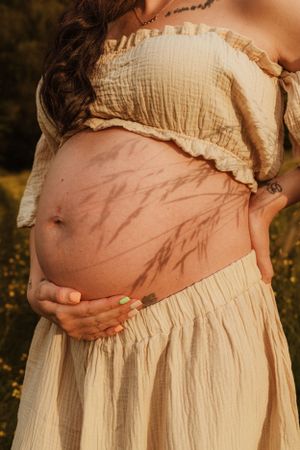 Close-up series of a pregnant belly in a cream dress against a backdrop of wildflowers.