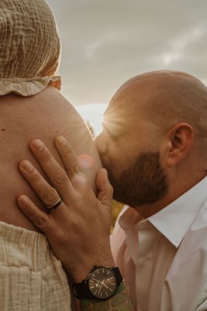 An intimate maternity moment captured with a gold watch and gentle touch against neutral fabric.