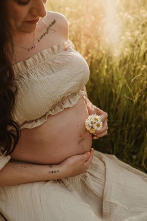 Serene maternity portrait with daisy flowers against glowing evening light.