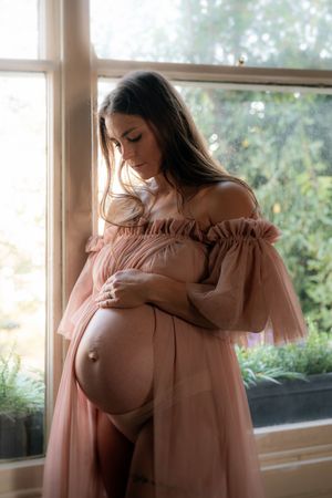A series of soft, romantic photos showing someone in a dusty pink off-shoulder dress by a sunlit window.