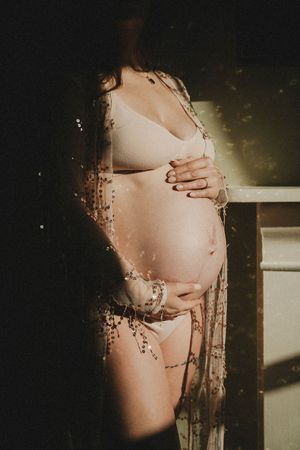 Artistic silhouette photography showing a pregnant belly with natural sunlight casting shadows through window glass.