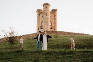 A stone castle tower stands atop a grassy hill while people explore the historic grounds on a cloudy day.