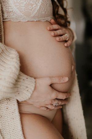 Close-up of hands gently cradling a pregnant belly while wearing a cozy white knit sweater.