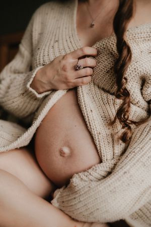Maternity photo series showing a growing baby bump in a cozy cream knit sweater against neutral tones.