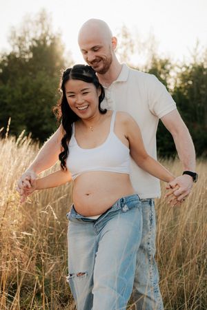 A couple shares a tender moment in a sunlit field of tall grass during a maternity photo session.