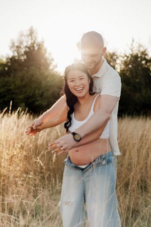 A couple embraces lovingly in a sunlit meadow of tall golden grass during a romantic photoshoot at sunset.
