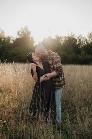 A couple shares a romantic moment in a golden sunlit field at sunset during a photo session.