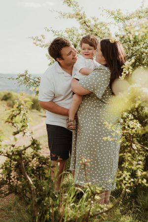 Family embraces tenderly in a sunlit garden setting wearing casual white and gray clothing.