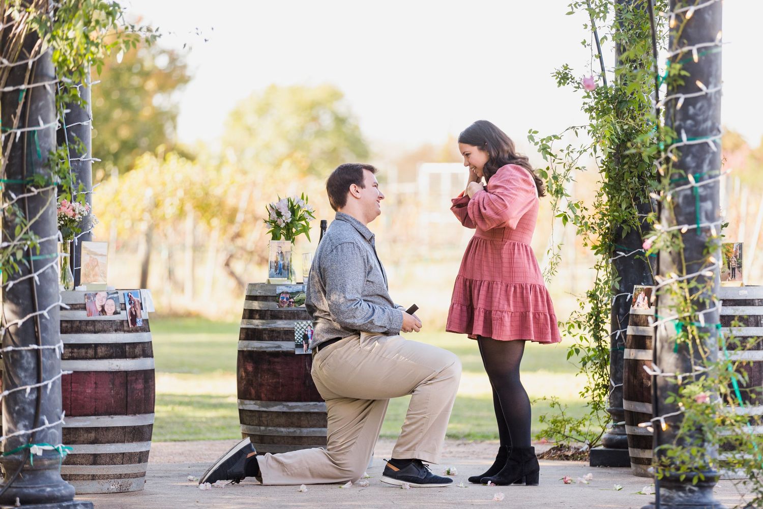 Romantic outdoor proposal scene with decorative lights and barrels.