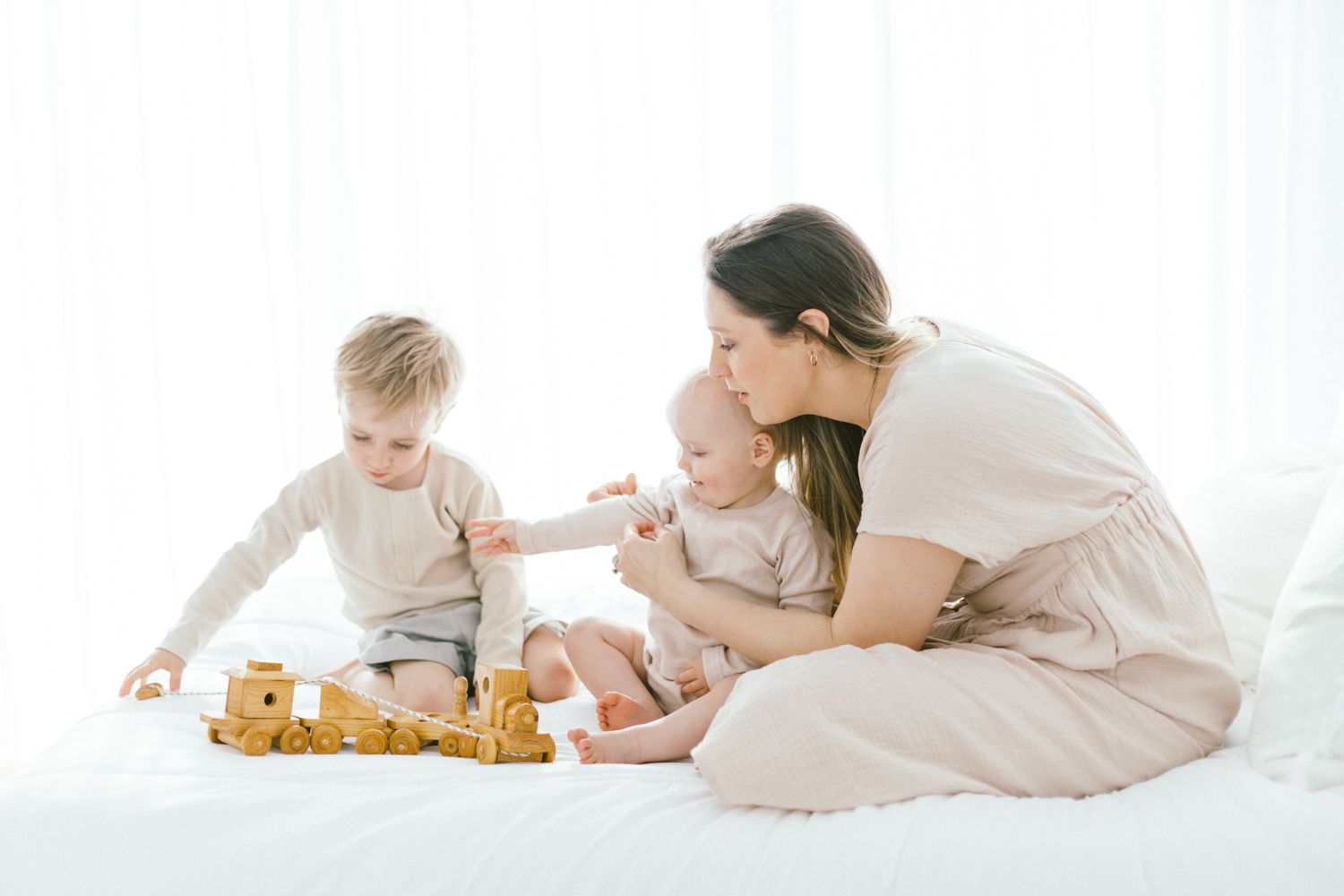 Parent and children playing together on crisp white bedding in natural light.