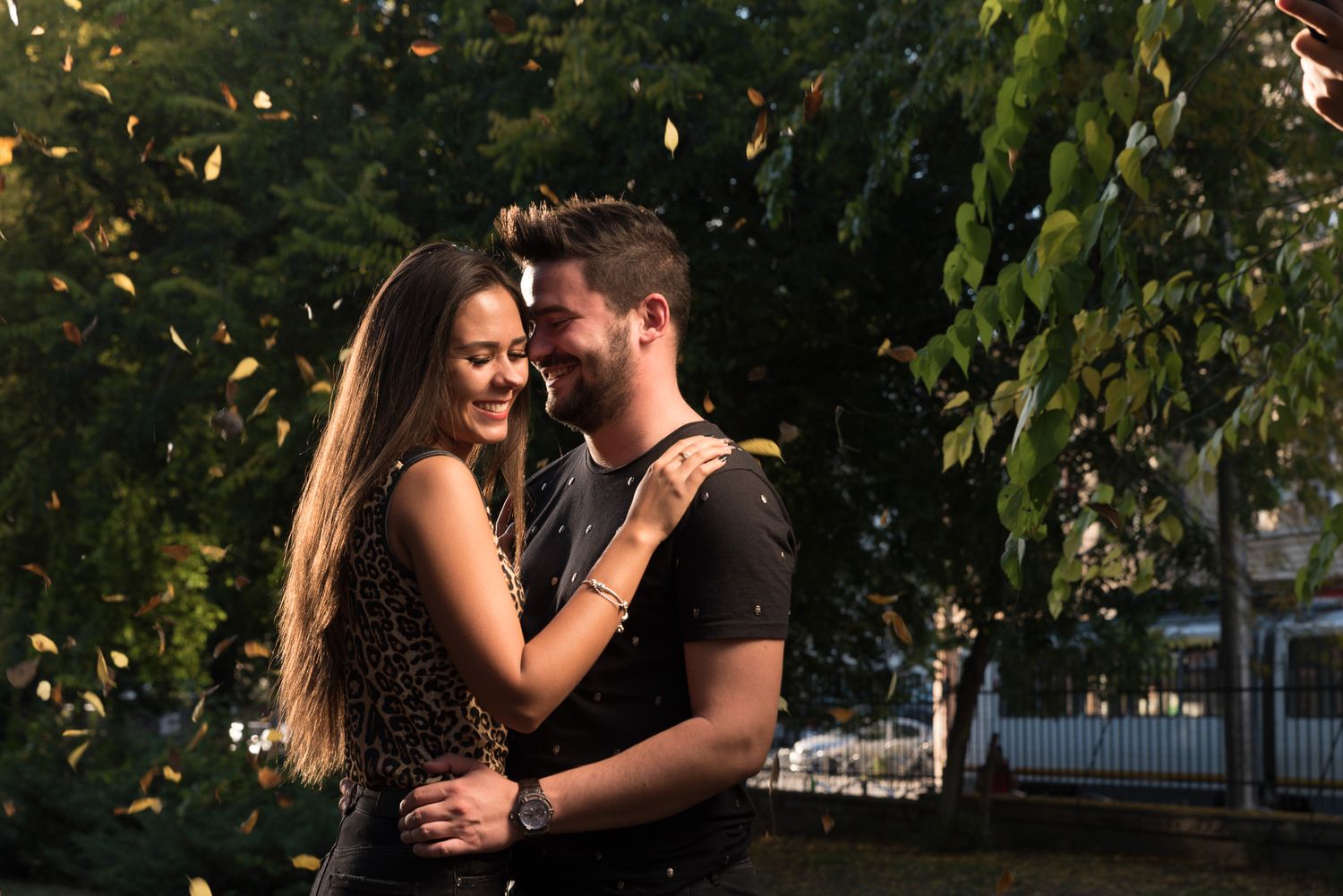 Couple embraces in golden sunlight among green foliage and trees.