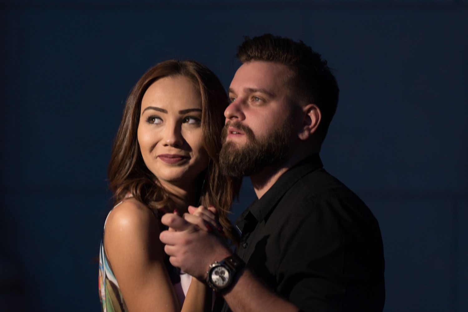 Intimate portrait against dark blue background with dramatic side lighting.