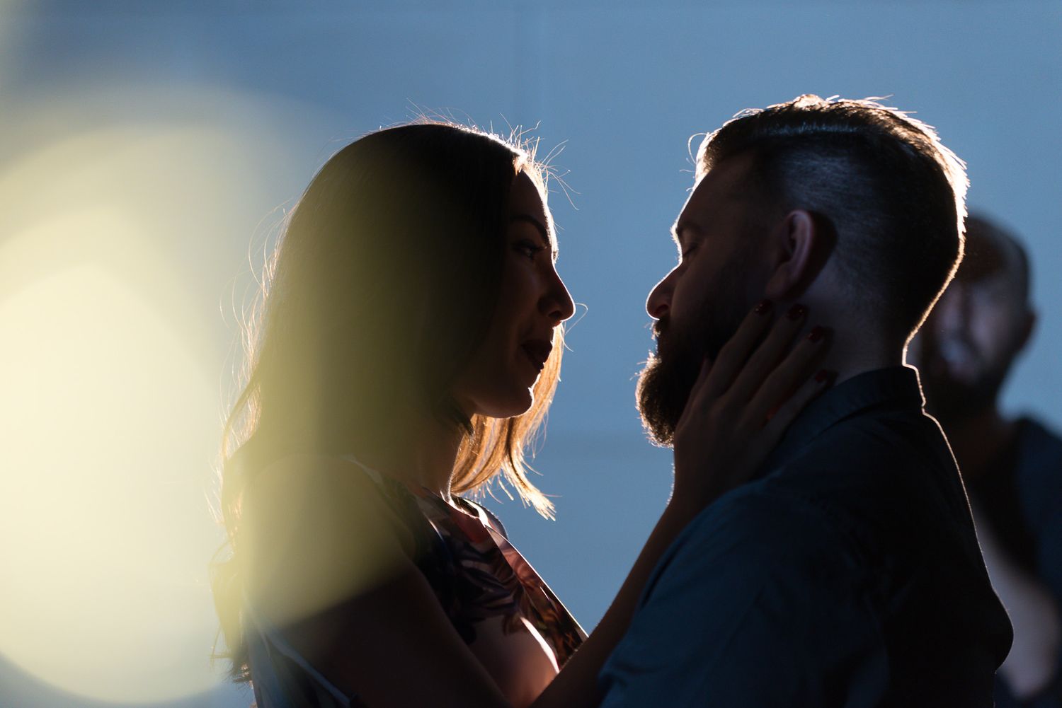 Backlit silhouette of couple against bright sky creating dramatic rim lighting effect.