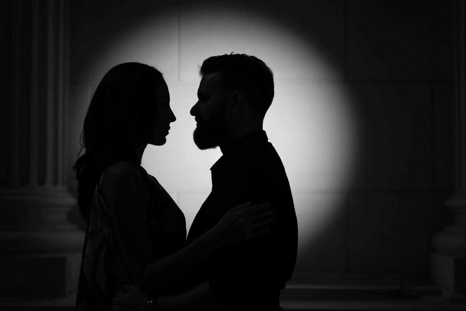 Silhouetted couple sharing an intimate moment against a dark background with dramatic lighting.